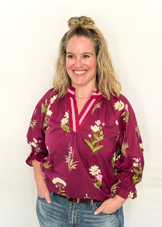 Plum top with florals in light pink and white with green leaves.  3/4 length sleeve and v-neck with contrast detail in plum and light pink. 