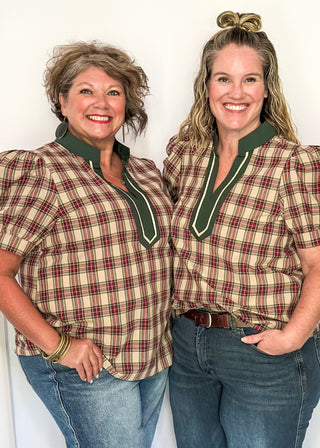 Two women wearing matching plaid shirts and jeans standing against a white background.