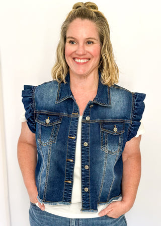 Sleeveless medium-wash denim button-up vest featuring ruffled shoulders, front button closure, chest pockets, and a raw hem 