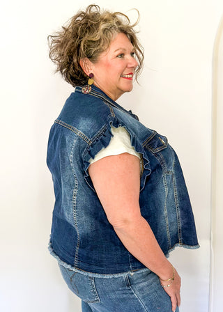 Sleeveless medium-wash denim button-up vest featuring ruffled shoulders, front button closure, chest pockets, and a raw hem 