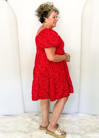 side view of woman wearing red jacquard babydoll dress with square neckline and short sleeves.