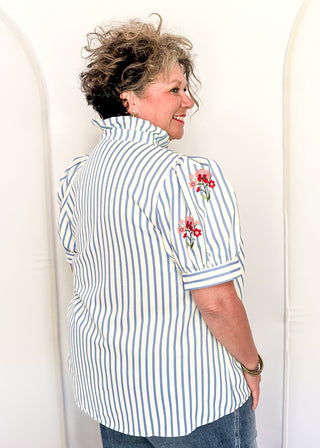 Short sleeve button up top with blue stripes and embroidered floral bundles in red and pink. 