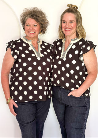 Women's black blouse with cream polka dots, striped split neckline, and flutter sleeves.