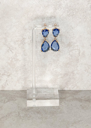 Blue teardrop dangle earrings displayed on a stand 
