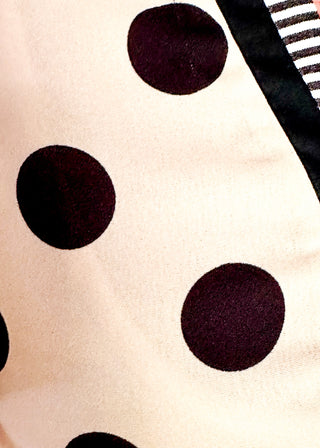 Close up of women's cream blouse with black polka dots, striped split neckline, and flutter sleeves.