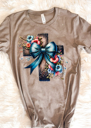 Stone colored tee with wooden cross with blue bow and pink and blue florals graphic and rhinestone detail.