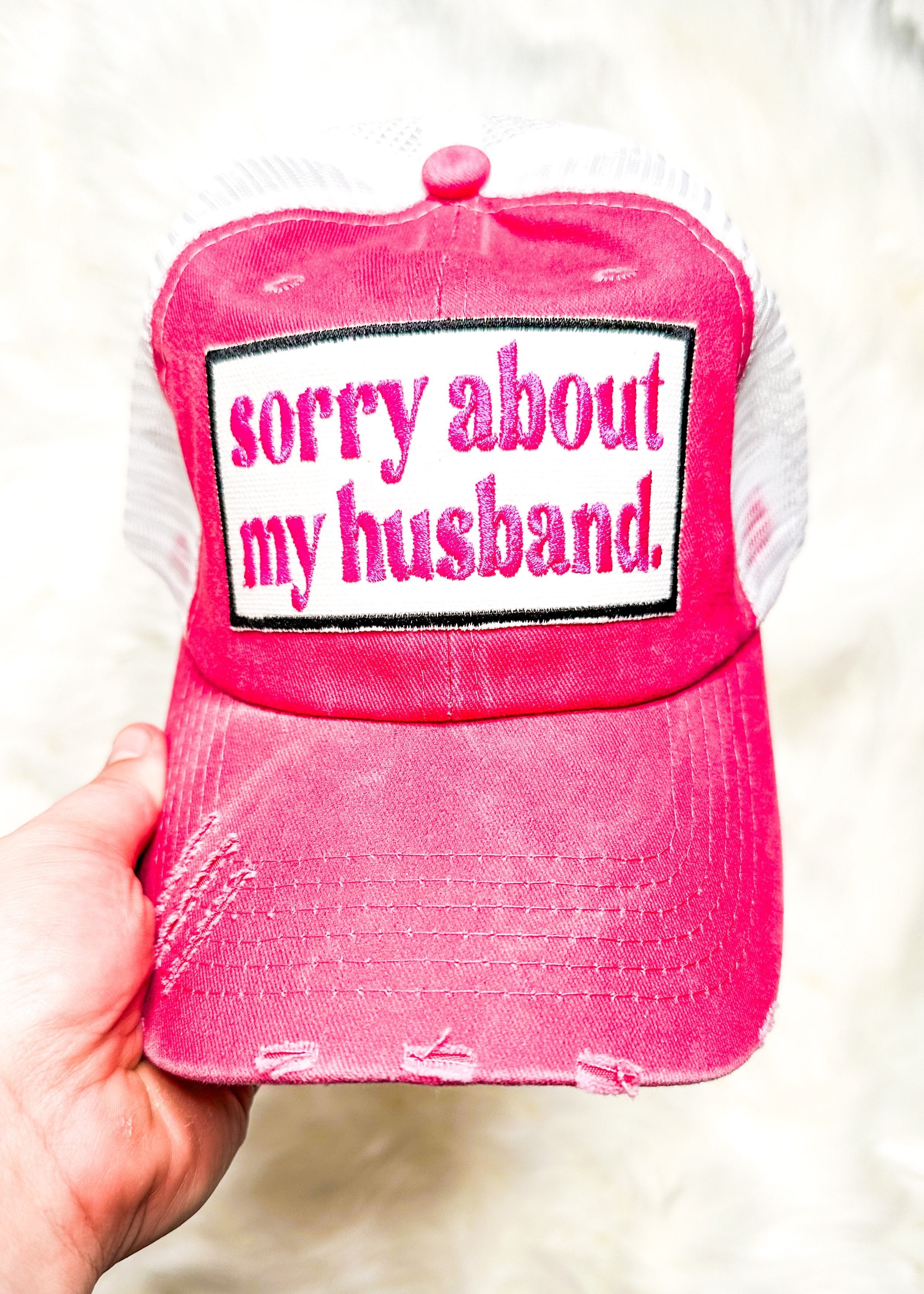 sorry about my husband embroidered in hot pink on white patch attached to a hot pink distressed trucker hat with white net back and velcro closure