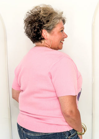 Back view of woman wearing a pink sweater with purple, orange, and light pink glitter pumpkins. 