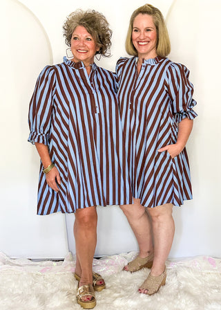 Two women modeling a brown and blue striped A line dress. 