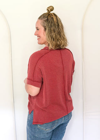 Woman wearing a red ribbed sweater and blue jeans against a white background