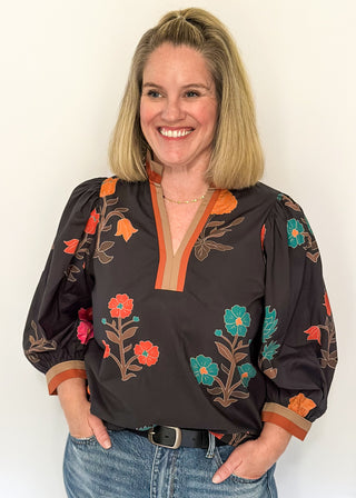 Black floral blouse with colorful flowers, contrast tan and orange trim, and ruffled neckline