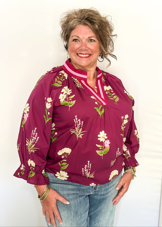Plum top with florals in light pink and white with green leaves.  3/4 length sleeve and v-neck with contrast detail in plum and light pink. 