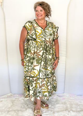 Ruffle cap sleeve maxi dress. off white background with green botanical print.  Dark green piping detail around v-neck, sleeves, bottom tier.  dark green ties on each side of waist. 