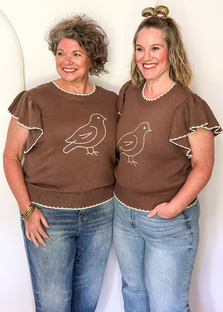 2 women wearing brown short sleeve sweater with white bird.