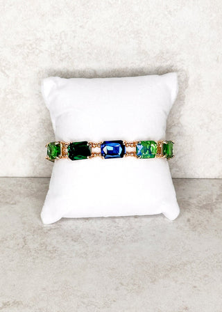 Green and blue gemstone bracelet with small gold beads displayed on a stand 