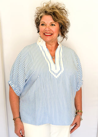 Striped seersucker top in light blue and white with short sleeves, relaxed fit, and split neckline.