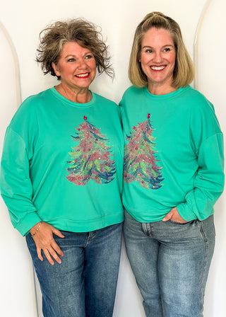 Two women wearing a long sleeve top in aqua with watercolor tree graphic and gemstone details.
