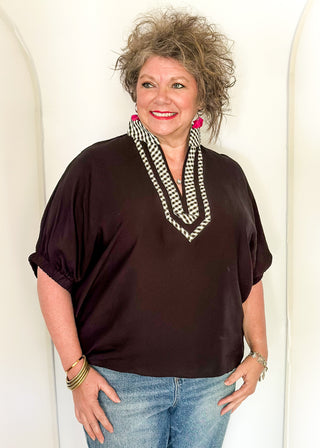 Women's black top featuring a gingham contrast neckline, loose silhouette, and subtle puff sleeves