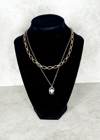 Gold chain necklace with a pendant on a black velvet stand against a white background