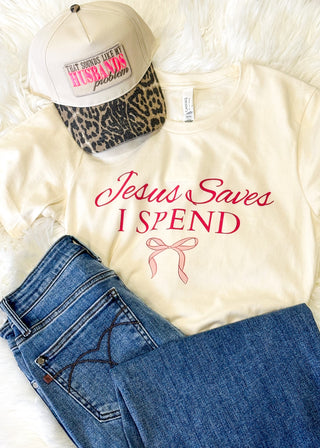 White t-shirt with 'Jesus Saves I Spend' text, blue jeans, and a cap with leopard print and pink text on a white background.