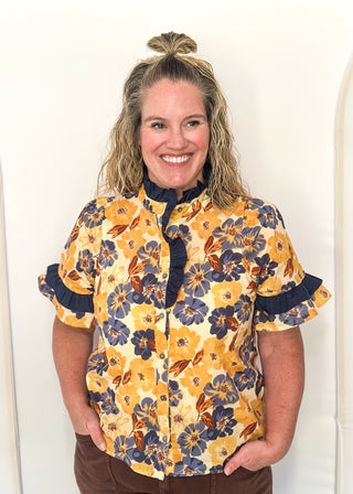 Bold Navy and golden blooms on this short sleeve top with navy ruffle detail on the sleeves, collar and 1/2 way down the front. Buttons up the front.