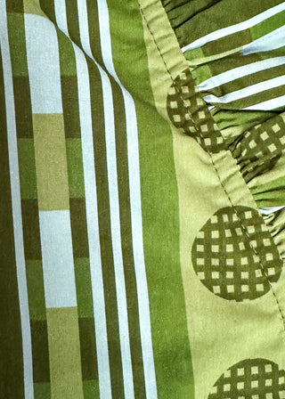 Close-up of a green and white patterned fabric with vertical stripes, a solid green stripe, and a ruffled border featuring green checkered circles.