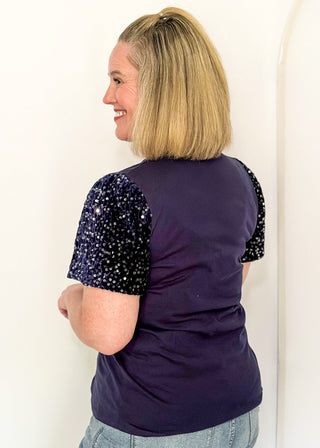 side view of woman wearing a navy short sequin sleeve top with plaid and green embellished trees