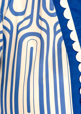 Close up of patterned short-sleeve top in blue with contrast trim with scallops, v-neckline.