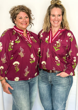 Plum top with florals in light pink and white with green leaves.  3/4 length sleeve and v-neck with contrast detail in plum and light pink. 