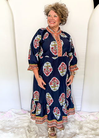Navy maxi dress with colorful floral medallion print, orange embroidered trim at neckline, and smocked cuffs