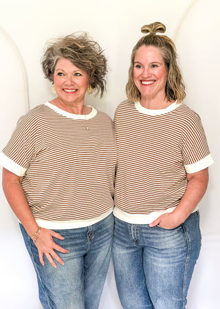 Two women wearing matching striped shirts and jeans against a white background