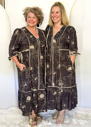 Black midi dress with cream piping and tie details on sleeves and waist.