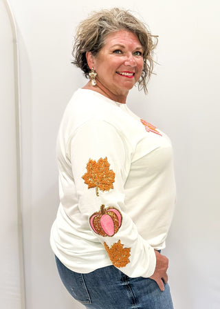 Light Ivory Long sleeve top with terracotta leaves and pink pumpkin patches sewn on the sleeves. "Thankful" chenille patches across the chest in pink and terracotta. 
