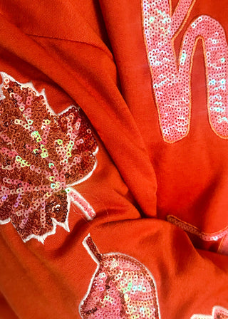 Close up of sequin detail on orange shirt.