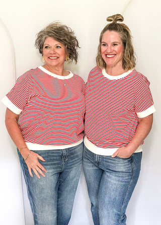 Two women wearing matching red and white striped shirts and blue jeans standing against a white background.