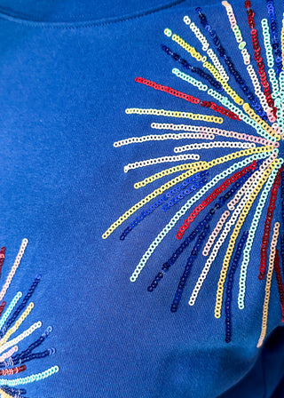 close up of blue short sleeve top with 2 sequin firework bursts.
