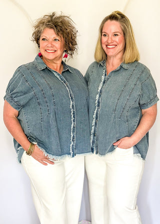 Denim button-down top with short sleeves, pointed collar, vertical stitched panels, and frayed raw-edge hem.