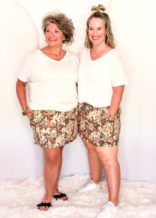 Two women wearing camo skorts with built-in shorts and pockets, paired with white tees.