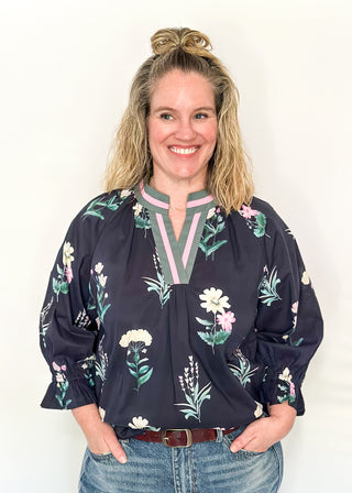 dark navy top with florals in light pink and white with green leaves.  3/4 length sleeve and v-neck with contrast detail in dusty blue and light pink. 