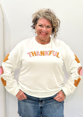 Light Ivory Long sleeve top with terracotta leaves and pink pumpkin patches sewn on the sleeves. "Thankful" chenille patches across the chest in pink and terracotta. 