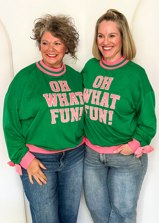 Two women wearing a green long sleeve mock neck top with pink contrast sleeve  and "OH WHAT FUN" embroidered letter patches.