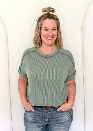 Woman wearing a green ribbed sweater and blue jeans against a white background