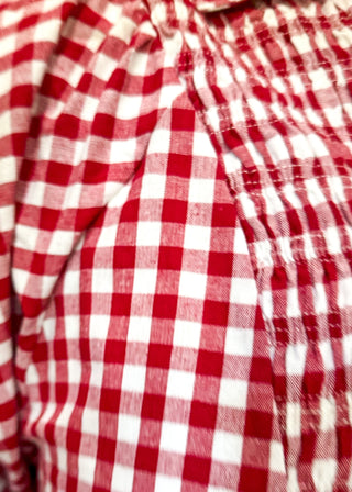 A close-up of a red and white gingham checkered top with a smocked chest pocket and short puff sleeves.