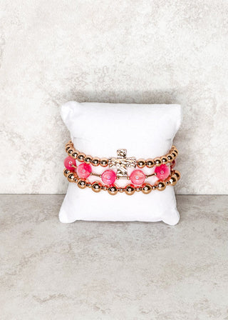 Set of pink beaded bracelets on a white jewelry cushion against a marble background