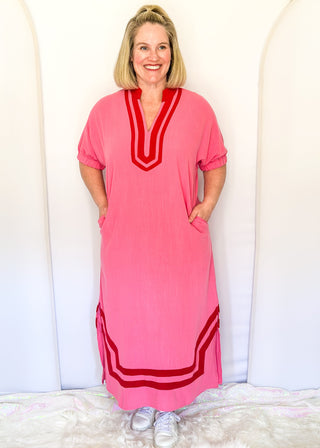 Pink midi-length dress with contrast red trim at neckline and hem, short sleeves with elastic, relaxed fit, and pockets.