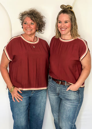 Two women wearing brick red tops with cap sleeves and crew necklines, styled with jeans.
