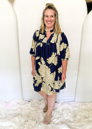 Woman wearing a navy floral dress standing on a white fluffy rug with a white wall background