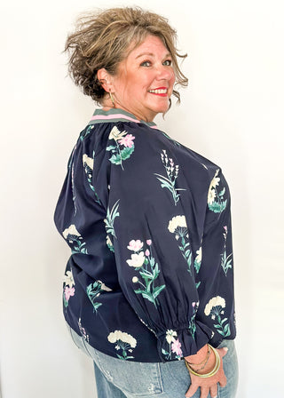 dark navy top with florals in light pink and white with green leaves.  3/4 length sleeve and v-neck with contrast detail in dusty blue and light pink. 