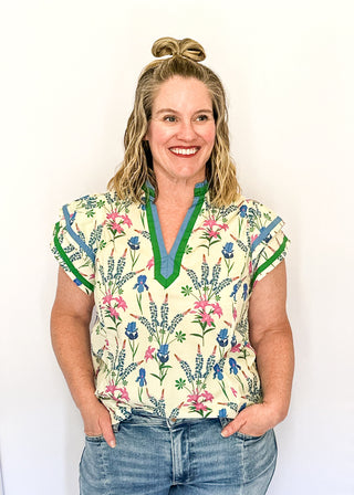 Cream short sleeve floral top with blue, pink, and green flowers, featuring a split V-neckline with green trim and a relaxed fit.