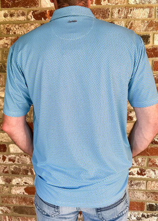 A man viewed from behind wearing a light blue short-sleeve polo shirt with a fine micro-dot pattern, standing against a rustic brick wall.
